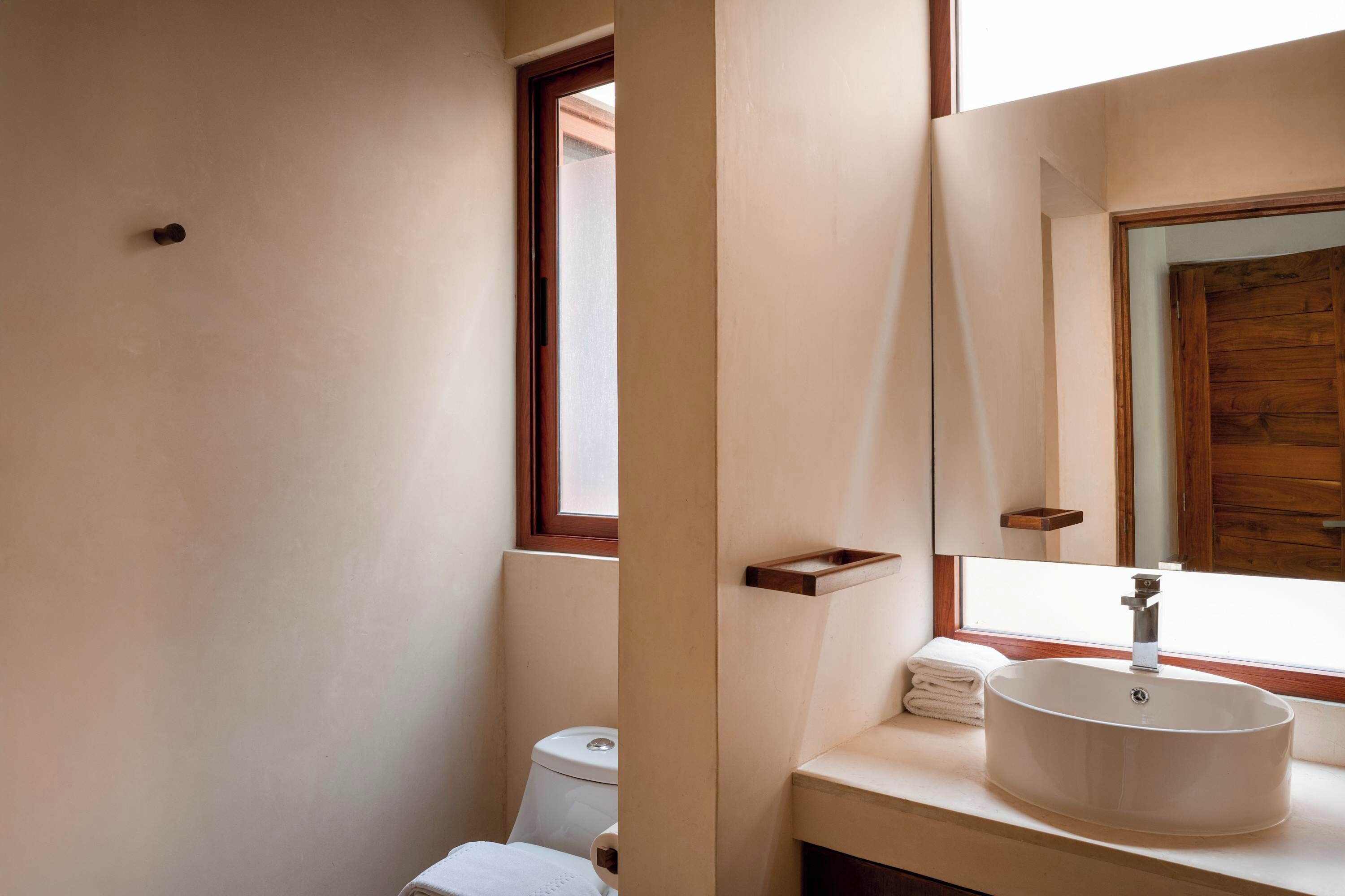 A bathroom with a white sink, a wooden window frame, and a mirror.