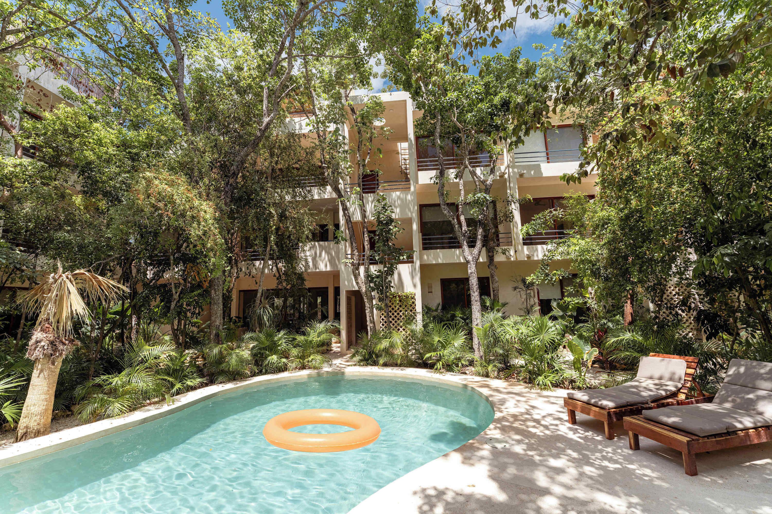 A pool with a floating ring, surrounded by lounge chairs and tropical plants.
