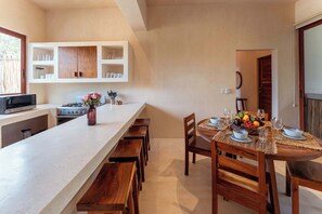 A kitchen with a long counter, wooden cabinets, and a dining area with a table set for four. - Ahal Holistika 3BR Oasis with Plunge Pool (Tulum)