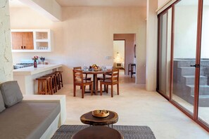 Een moderne woonkamer met een bank, een eettafel met stoelen, een keuken met kasten en een fornuis, en een balkon met een schuifdeur.