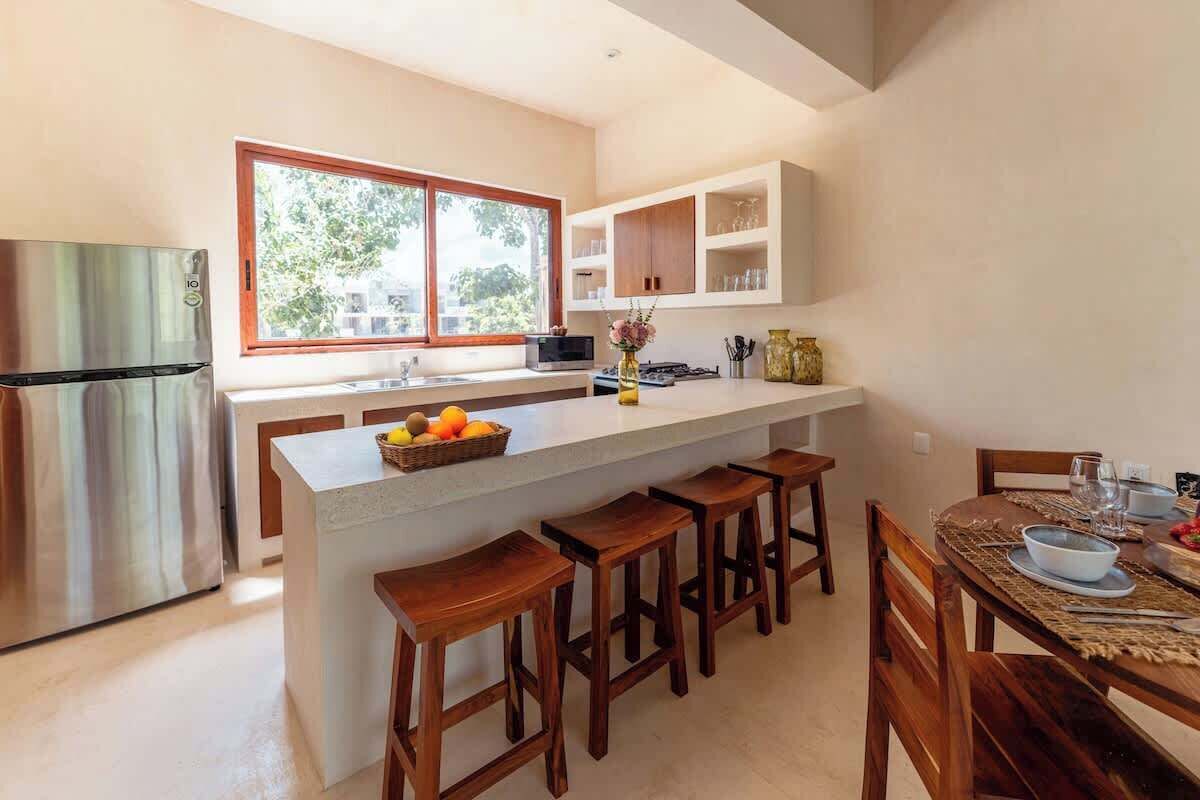 Uma cozinha moderna com uma ilha grande, banquetas de madeira e uma mesa de jantar posta para quatro pessoas.