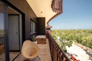 Ein Balkon mit Blick auf eine grüne Landschaft, ein Korbstuhl und ein Topfpflanze.