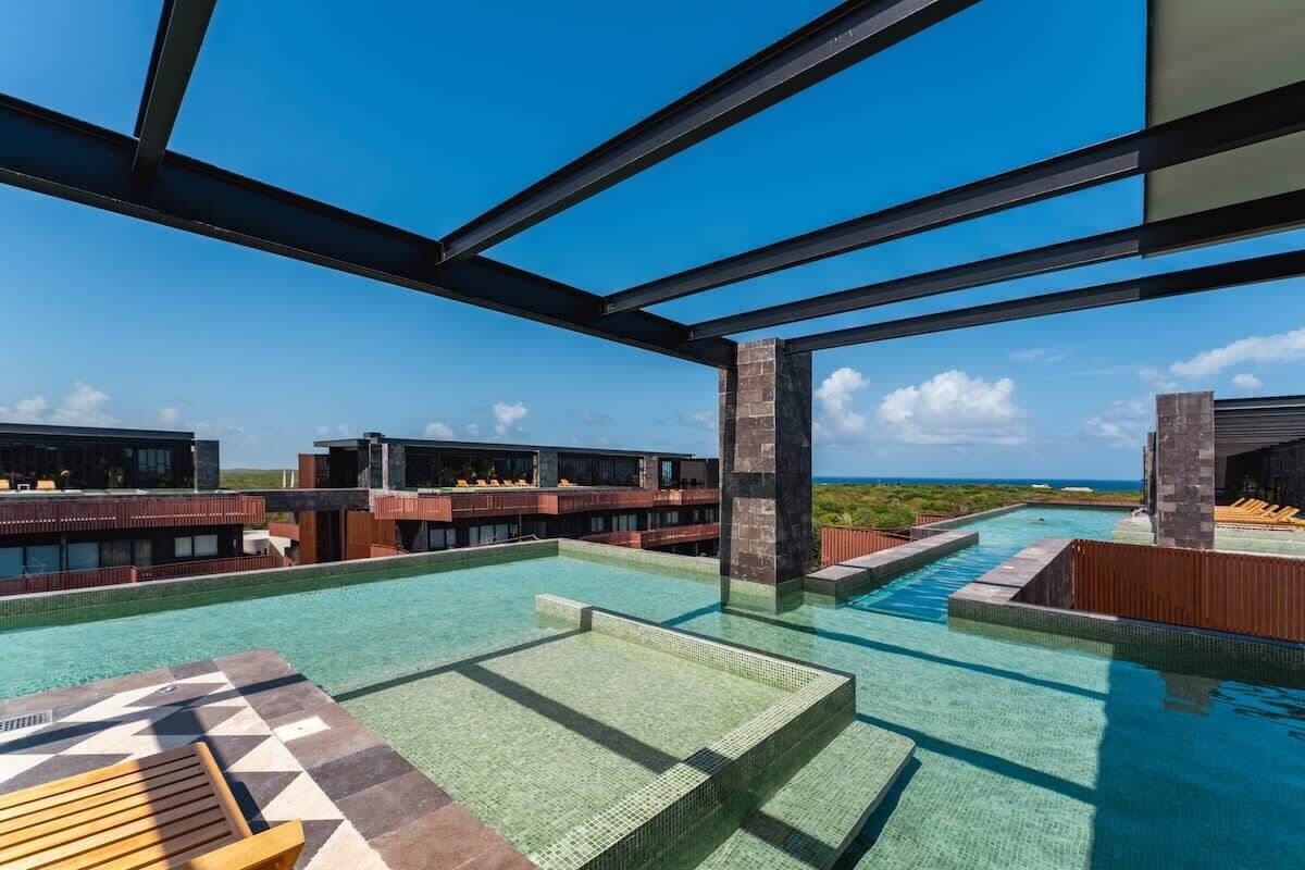 Une piscine à débordement située sur le toit, avec une eau d’un bleu cristallin, une terrasse en bois et une vue sur l’océan.