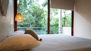 A bed with white bedding, a hanging light fixture, and a view of trees through a balcony. - Elegant 3BR Penthouse – Rooftop Pool & Jungle View (Tulum)