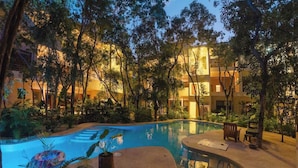 A pool area with a curved edge, surrounded by trees and a building in the background. - Elegant 3BR Penthouse – Rooftop Pool & Jungle View (Tulum)