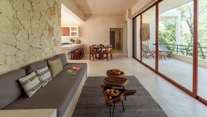 Un interior moderno con pared de piedra, un sofá con cojines, un comedor y un balcón con mobiliario exterior.