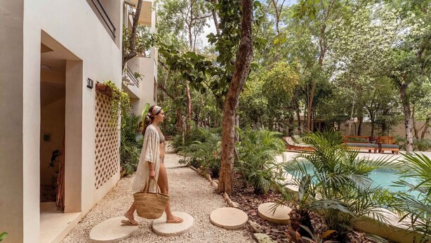 A pathway leading to a pool area with a person walking, surrounded by greenery and a building with a lattice design. - Stylish Ground-Floor 3BR Haven ,Luxe Plunge Pool (Tulum)