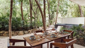 An outdoor dining area with a wooden table set for four, surrounded by chairs, with a stone wall and trees in the background. - Stylish Ground-Floor 3BR Haven ,Luxe Plunge Pool (Tulum)