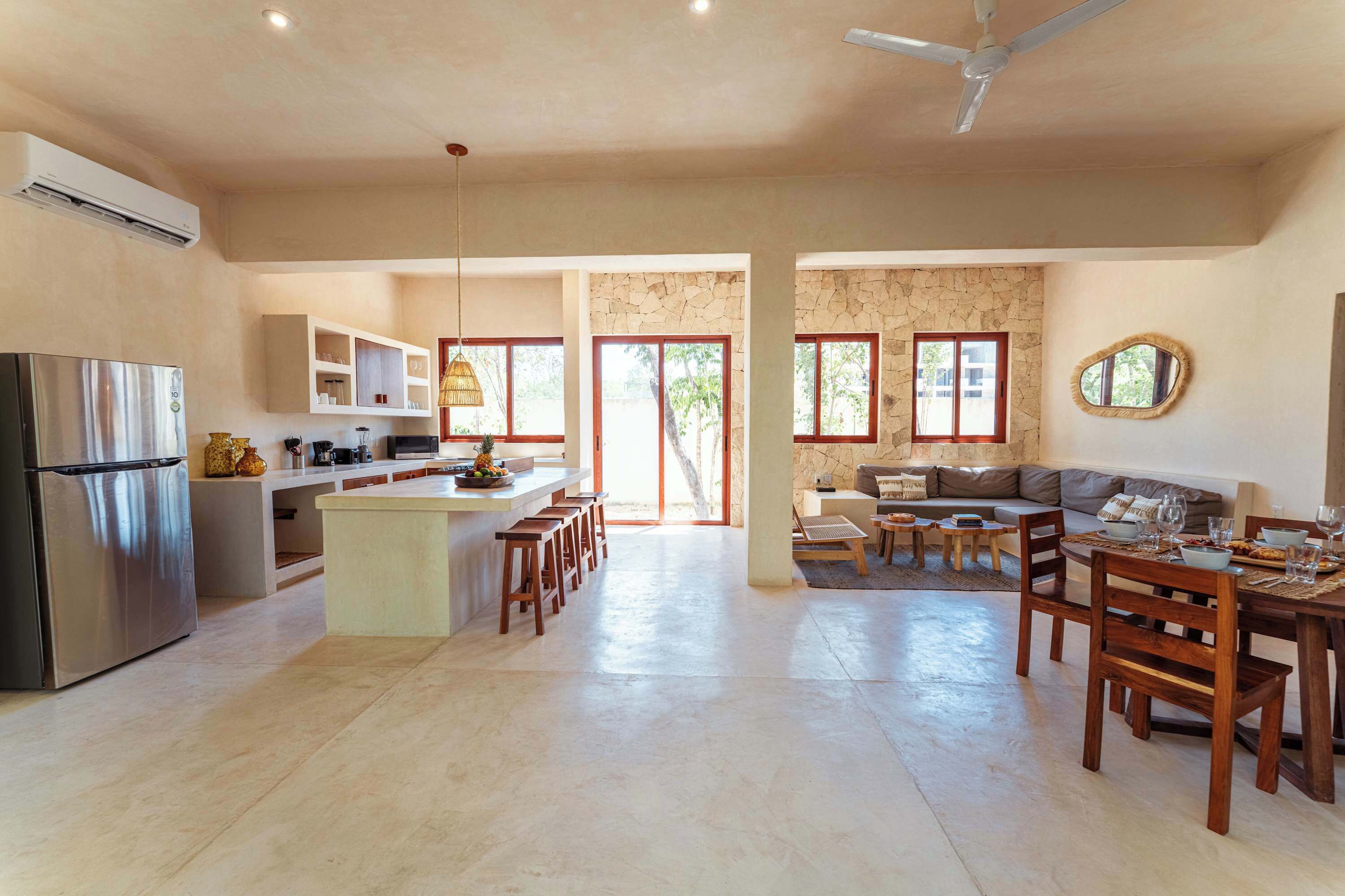 Una cocina amplia con una isla central, un comedor con sillas de madera y una sala de estar con sofá y televisor.