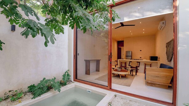 Ein modernes Interieur mit einer Glastür, die in einen Essbereich führt, einem kleinen Pool und einer durch die Glaswand sichtbaren Küche.