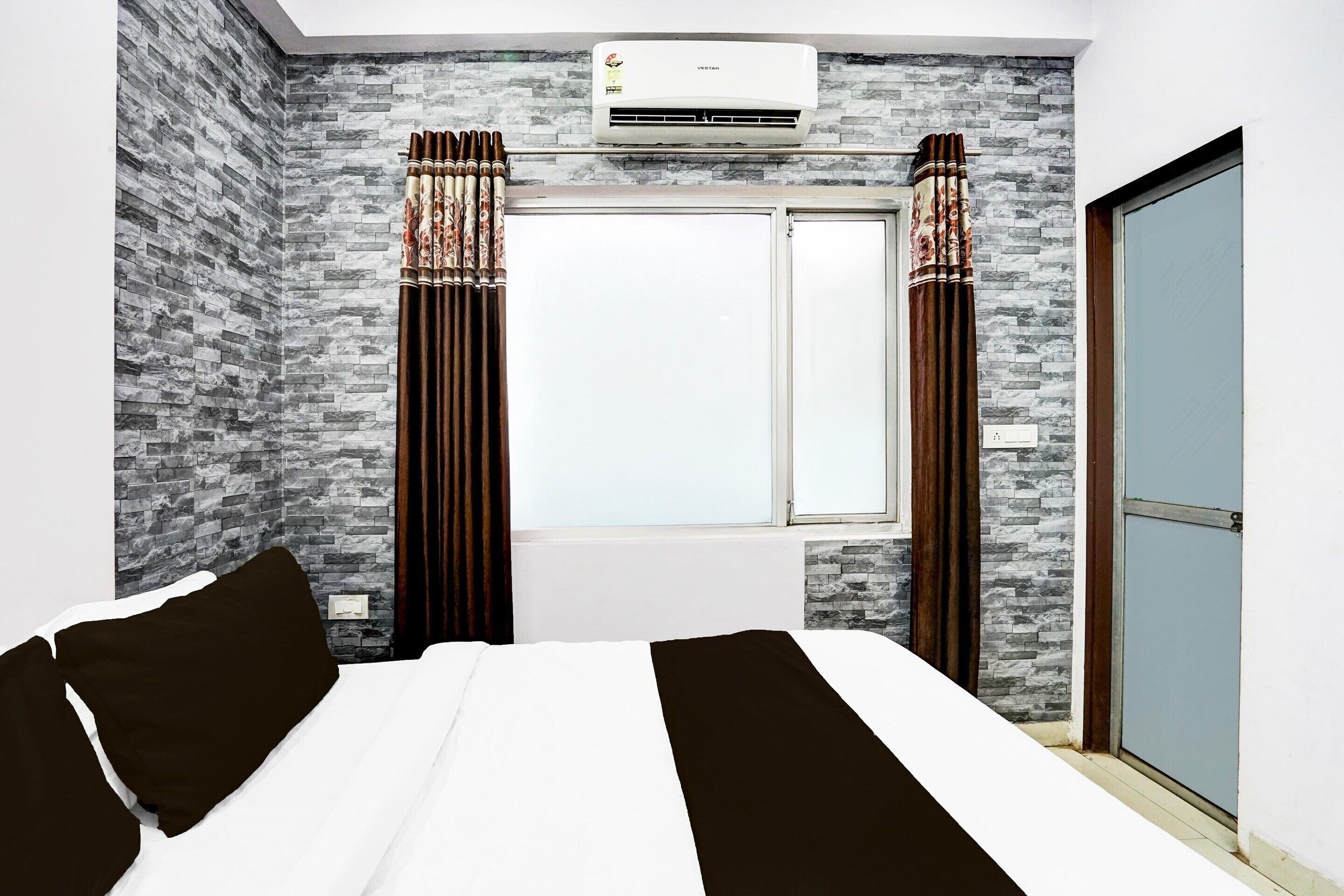 A hotel room with a bed, curtains, an air conditioning unit, and a window.