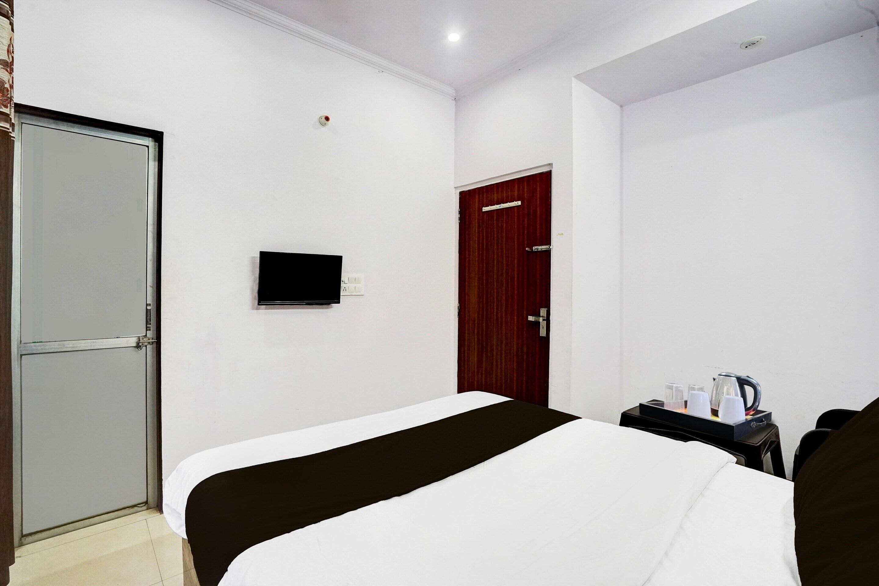 A hotel room with a bed, a TV, a wooden door, and a small table with a tray of items.
