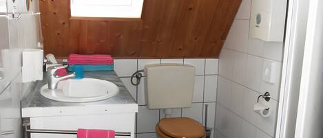 Une petite salle de bain avec un plafond en bois, un lavabo blanc, des toilettes et une fenêtre.