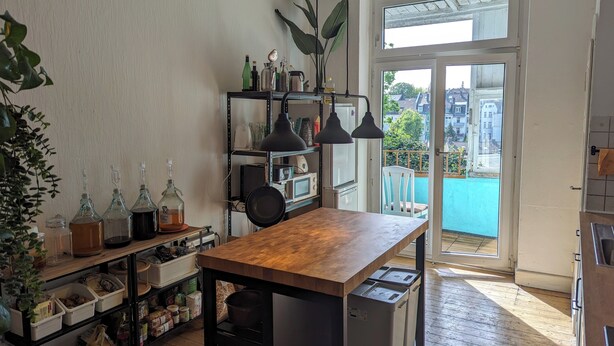 A kitchen with wooden countertops, a black hanging lamp, and a view of a balcony with a blue railing. - Cozy old building with sauna and view (Wuppertal)