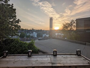 A rooftop terrace with a view of a sunset over a residential area, including a tall chimney and a row of houses. - A cozy historic building with a sauna and a view (Wuppertal)
