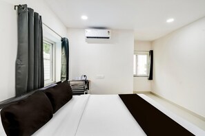 Ein Hotelzimmer mit einem Bett, einem Vorhangfenster, einer Klimaanlage und einem kleinen Tisch mit Wasserkocher.