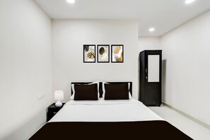 Ein Hotelzimmer mit einem Bett, einem Nachttisch, einer Lampe, einem Kleiderschrank und drei gerahmten Kunstwerken an der Wand.