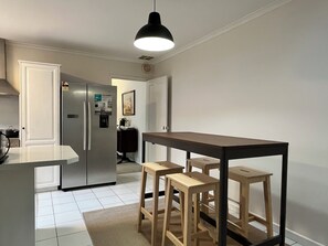 Una cocina moderna con refrigerador, una mesa de comedor con taburetes y una lámpara colgante.