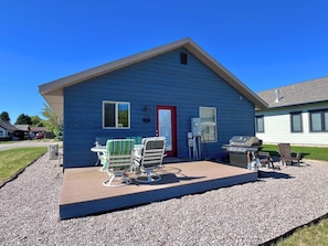 Een blauw huis met een rode deur, een terras met een tafel en stoelen, en een barbecue.