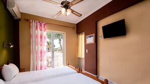 Quarto de hotel com cama, ventoinha no teto, ar condicionado e televisão presa à parede.