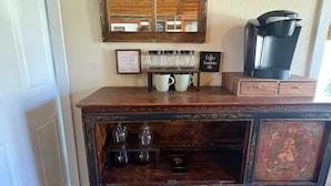 Een rustiek houten kastje met glaswerk, een koffiezetapparaat en een ingelijste bord op de muur.