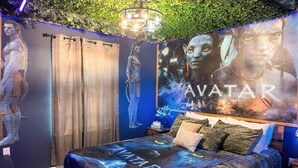 Quarto com cama, cortinas, um candelabro e um mural na parede.