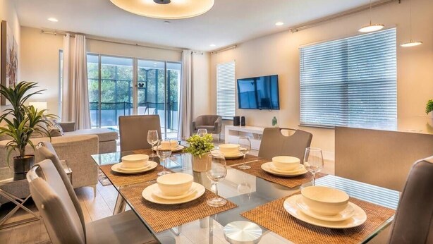 Een moderne eethoek met een glazen tafel, stoelen en een centraal hanglamp.