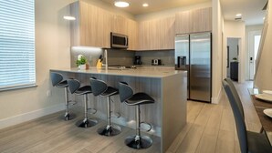 Een moderne keuken met een centraal eiland, barstoelen, roestvrijstalen apparatuur en houten kasten.