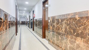 A corridor with marble walls and doors, a fire extinguisher, and a ceiling light. - Deluxemahipalpur Near Airport (New Delhi)