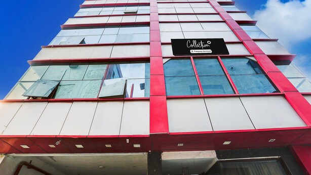 A multi-story building with a prominent red and white facade, large windows, and a sign indicating it is a company serviced hotel. - Deluxemahipalpur Near Airport (New Delhi)