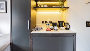 A compact kitchenette with a countertop, a coffee maker, a kettle, a bowl, and a towel.