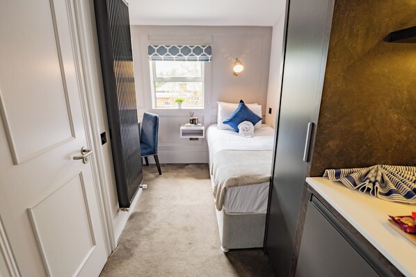 A narrow hallway leading to a bedroom with a bed, a nightstand, a chair, and a window with a view. - Cozy Suite in Rathmines | Walk to City Centre (Dublin)