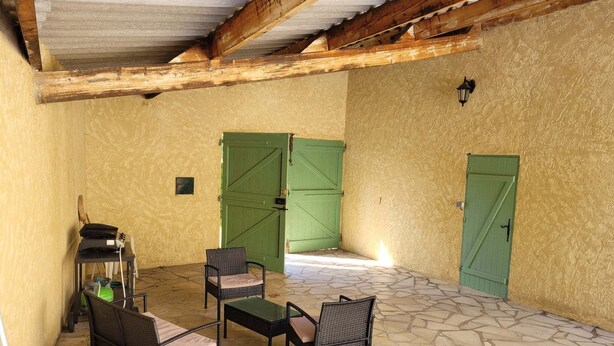 A covered patio with stone flooring, two green doors, wicker furniture, and a small table. - Vacation home with private pool (Banon)