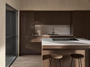 A modern kitchen with a white countertop, dark wooden cabinets, and two stools.