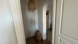 Um corredor com soalho de madeira, uma porta branca e um candeeiro suspenso.