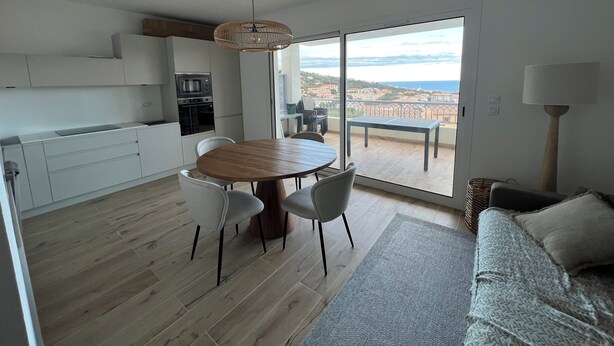 Cozinha moderna com área de jantar, sofá e vista para o mar.
