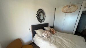 Quarto com cama, cadeira, espelho e luminária pendente.