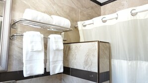 A bathroom with a shower, a towel rack with multiple towels, and a marble wall.