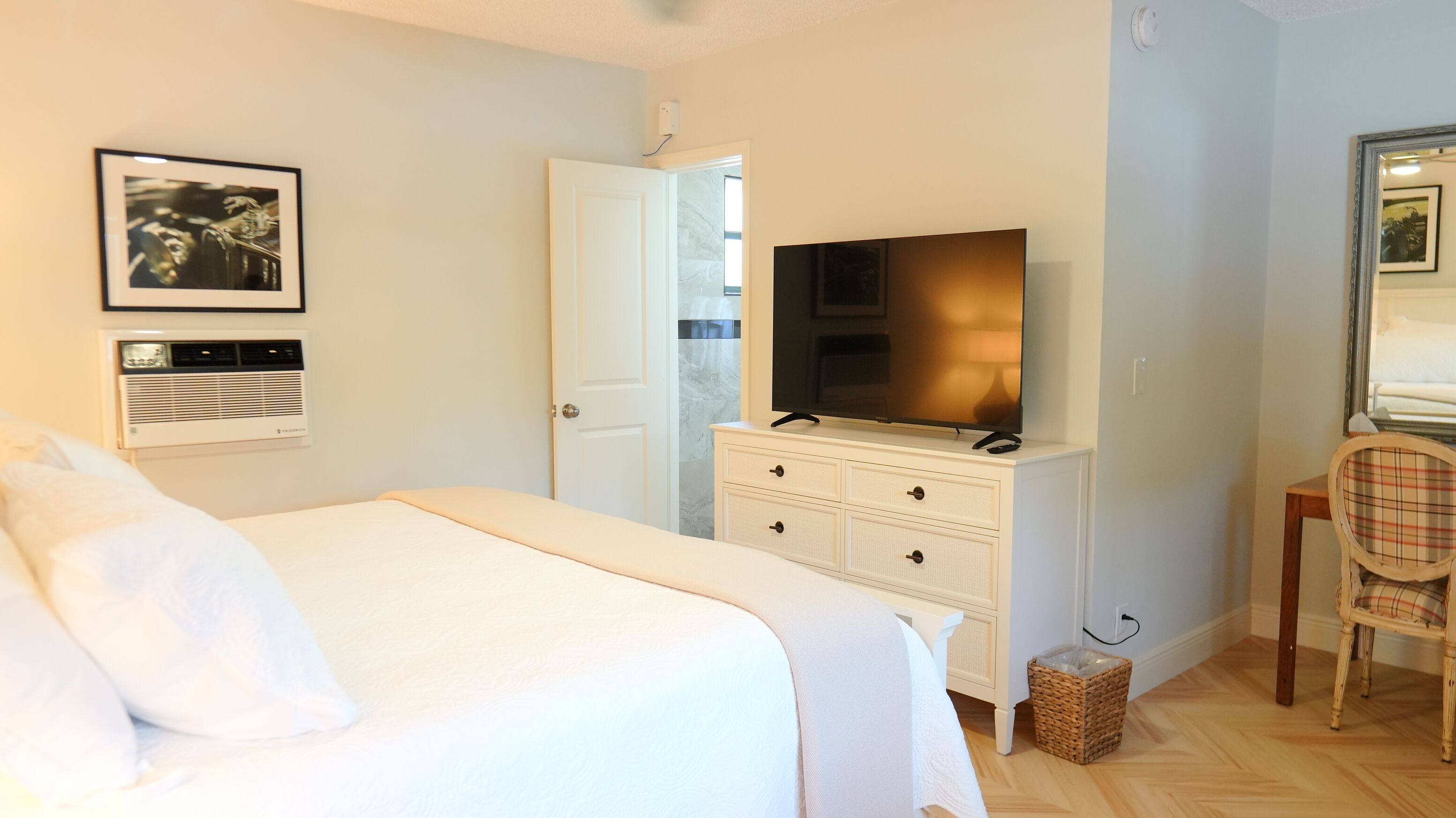 Habitación de hotel con una cama, un televisor en una cómoda, una silla y un cuadro en la pared.