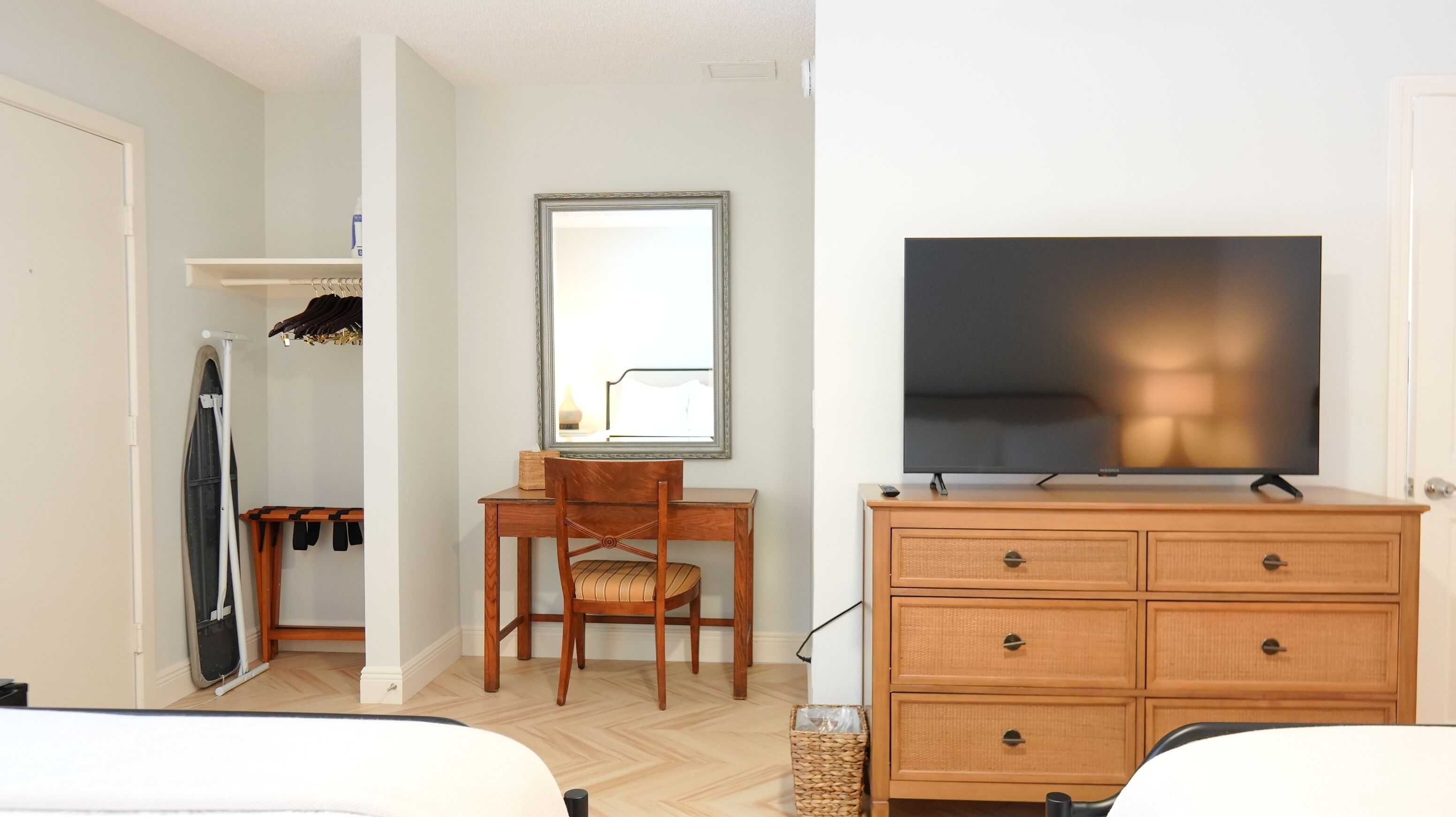 A hotel room with a bed, a desk with a chair, a television, a wardrobe, and a mirror.