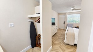 A bedroom with a bed, a dresser, a hanging garment, and a radiator. - The Palm Rose  (West Palm Beach)