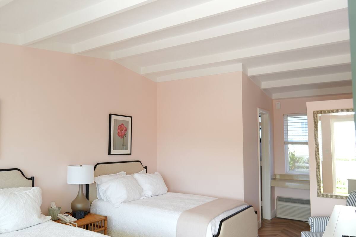 Ein Schlafzimmer mit zwei Betten, einem Nachttisch mit Lampe und gerahmten Blumenbildern an der Wand.