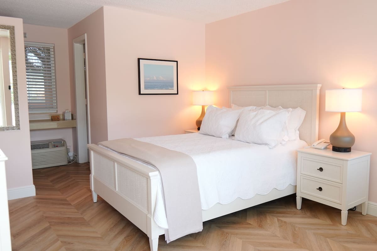 Ein ordentlich eingerichtetes Schlafzimmer mit Bett, Nachttischlampen, einem Telefon am Nachttisch und einem gerahmten Bild an der Wand.