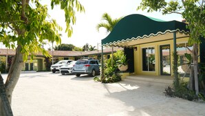 A building with a green awning, a parking area with three cars, and a palm tree.