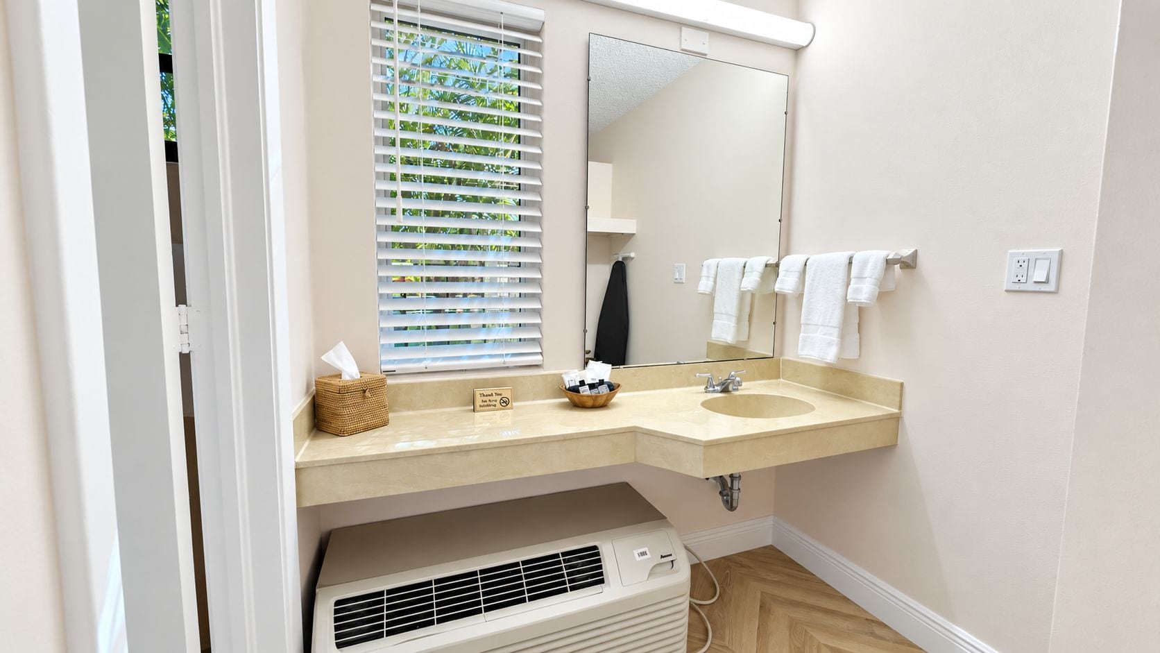 Un baño con un lavabo color beige, un espejo y una ventana con persianas.