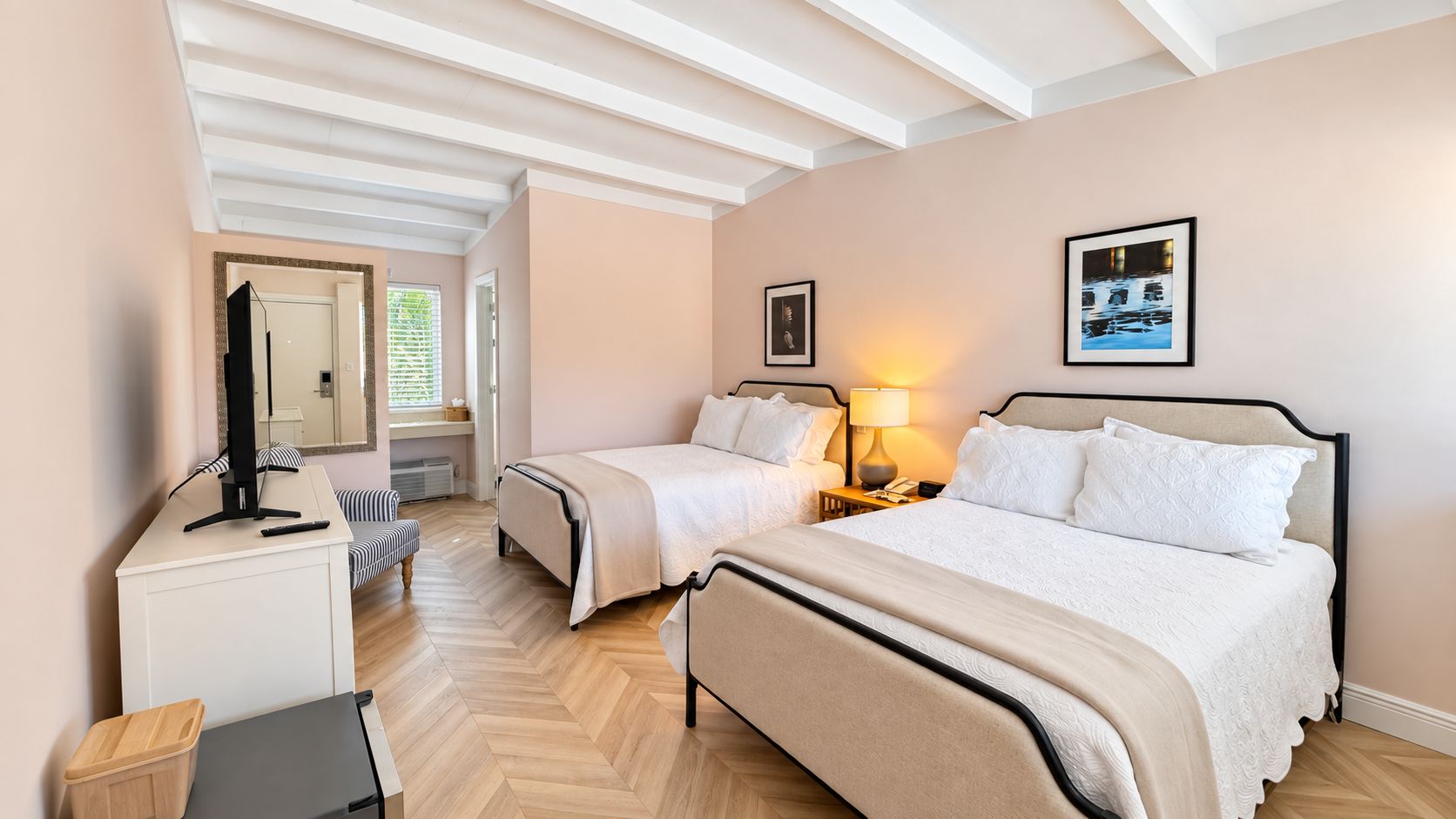 Habitación de hotel con dos camas, un escritorio, una silla, un espejo y una ventana con persianas.
