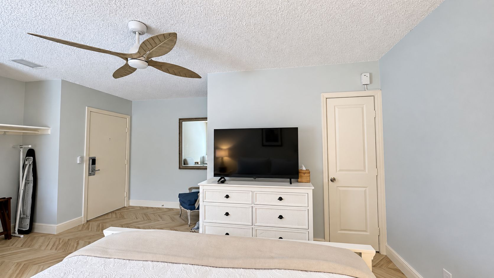 A bedroom with a bed, a dresser, a television, a ceiling fan, and a door.