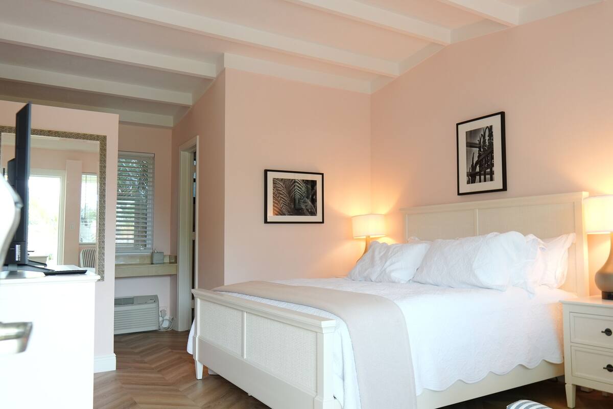 Ein Schlafzimmer mit einem Bett, Nachttischlampen, einem Beistelltisch und einem gerahmten Bild an der Wand.