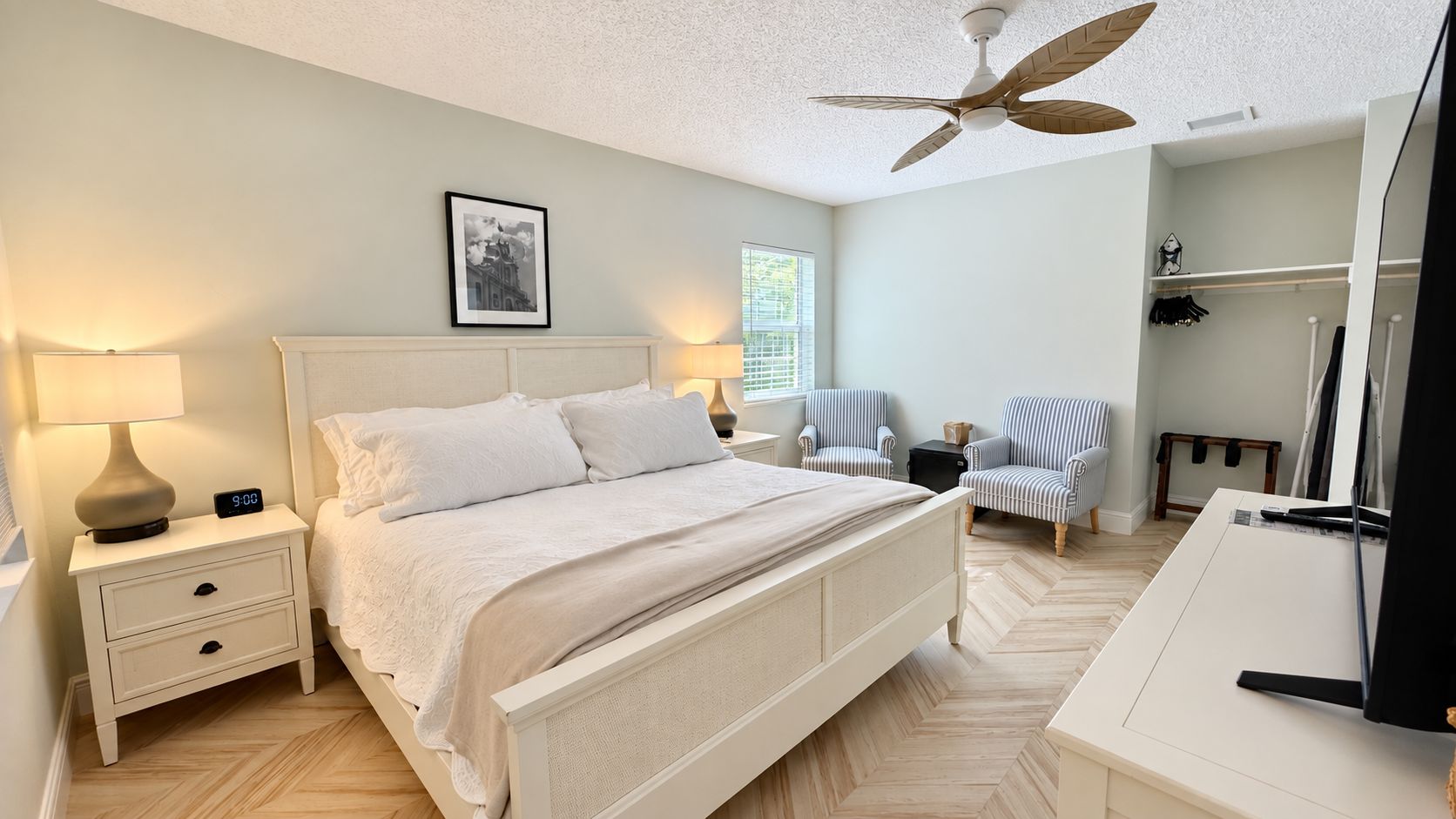 A bedroom with a bed, nightstands, a desk, a chair, a ceiling fan, and a window.