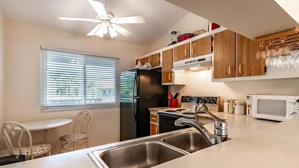 Une cuisine équipée d’un évier à deux bacs, d’un réfrigérateur, d’une cuisinière et d’un ventilateur de plafond.